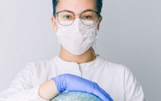 Woman in face mask, gloves, and surgical scrubs holding globe