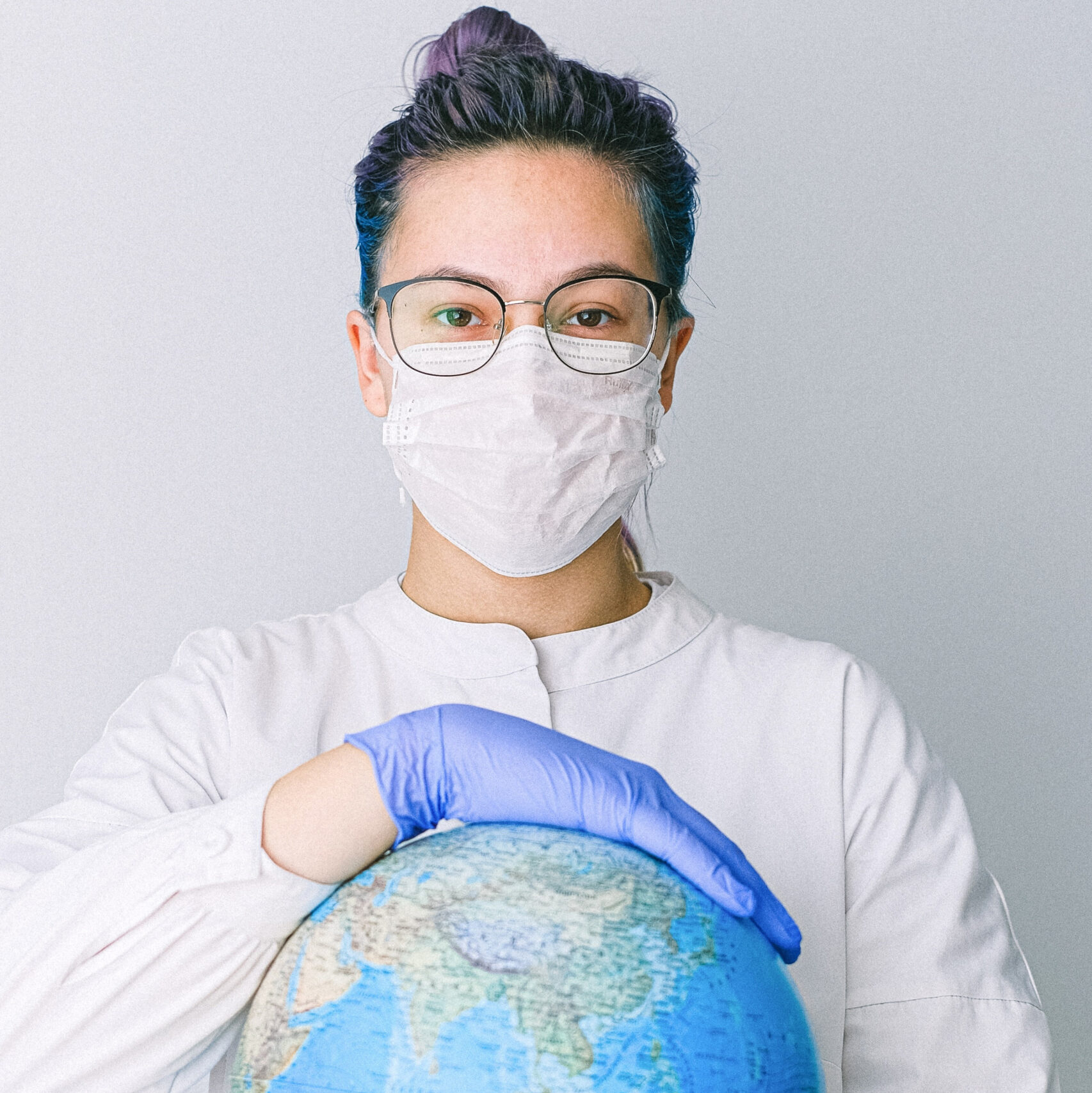 Woman in face mask, gloves, and surgical scrubs holding globe
